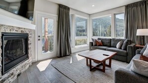 Ein geräumiges Wohnzimmer mit Kamin, großen Fenstern, einer Couch und einem Couchtisch.
