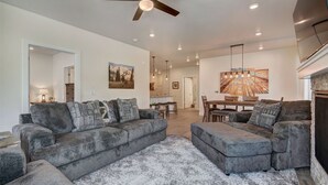 Ein modernes Wohnzimmer mit grauen Sofas, einem großen Teppich und einem Deckenventilator.