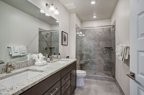 A modern bathroom with a double sink vanity, a glass shower enclosure, and a toilet.