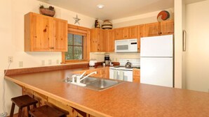 A kitchen with wooden cabinets, a stainless steel sink, a microwave, and a refrigerator. - R&R for 6 | Prime Location + Exclusive Privacy! (Keystone)