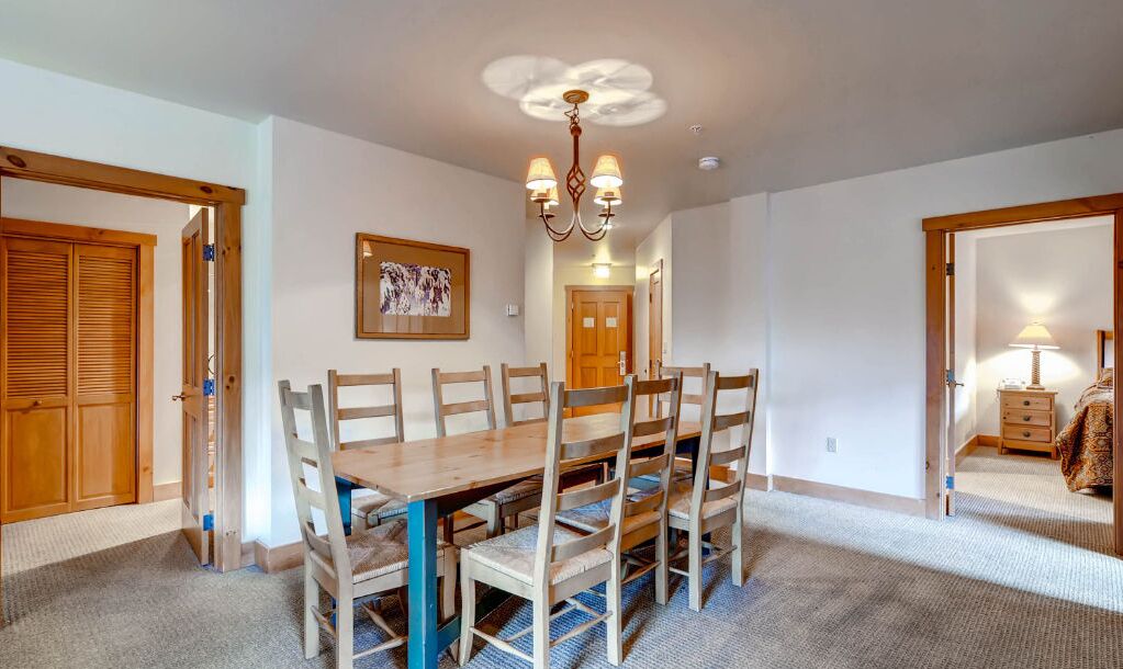 A dining room with a wooden table and chairs, a chandelier, and a framed picture on the wall.