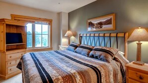 Une chambre à coucher avec un lit, une armoire en bois, une télévision, des lampes de chevet et un tableau au mur.