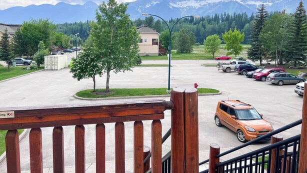 A parking lot with cars, a building, and mountains in the background. - Hotel Style 1 Bedroom & Bathroom (Fernie)