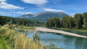 A river with a mountain in the background, surrounded by greenery. - Hotel Style 1 Bedroom & Bathroom (Fernie)