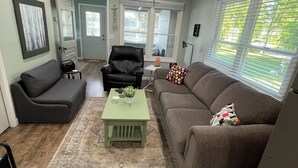 Ein Wohnzimmer mit einem grauen Ecksofa, einem schwarzen Ledersessel, einem grünen Couchtisch und einem gemusterten Teppich.