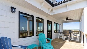 Terraza cubierta al aire libre con sillas Adirondack y una mesa, con vista a la playa.