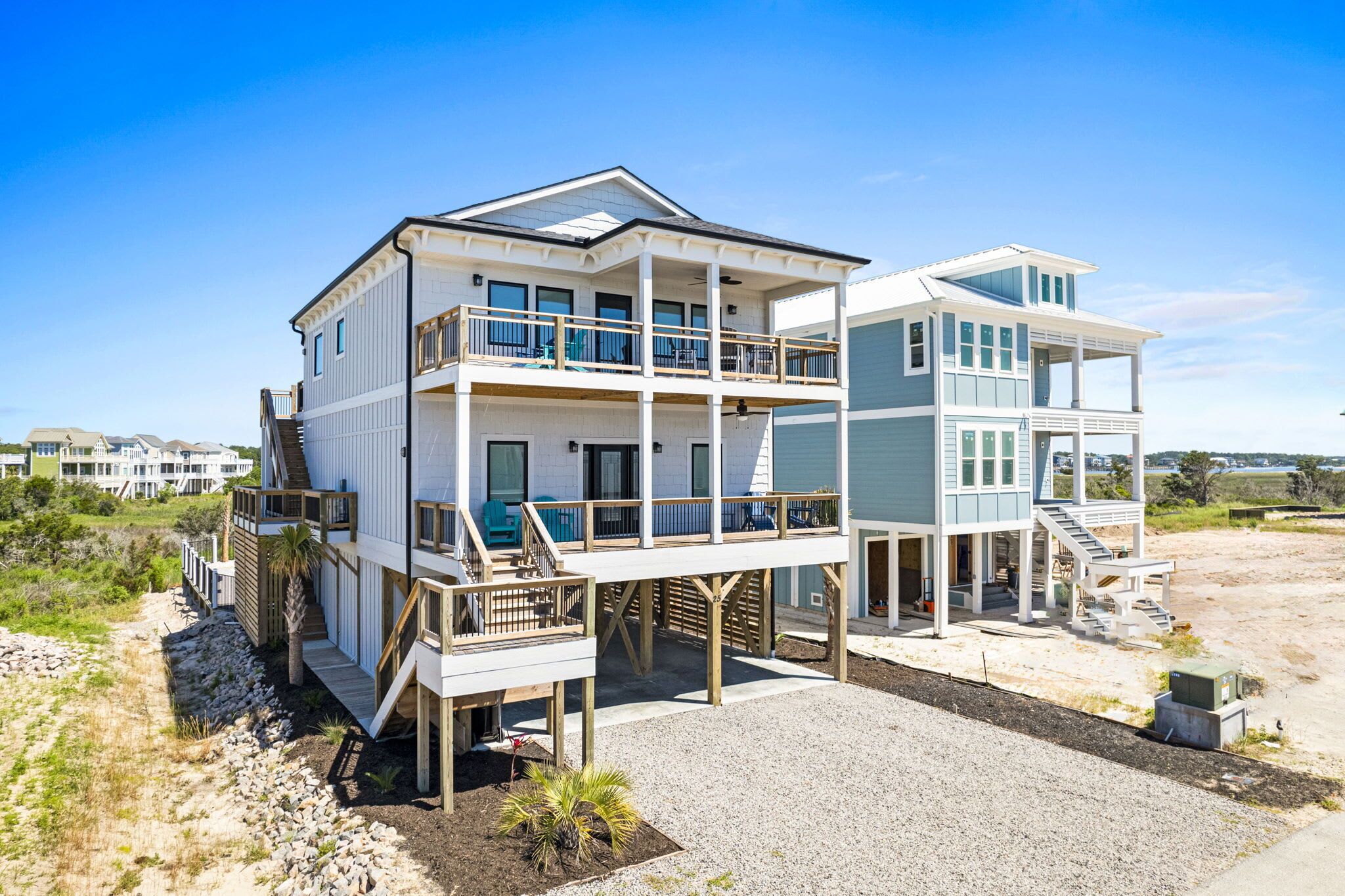 Una casa frente a la playa de varios pisos con balcón, porche cubierto y una escalera que lleva a los niveles superiores.