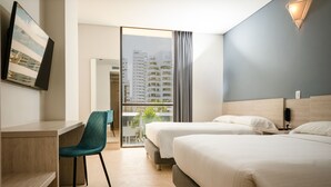 A hotel room with a desk, two beds, a chair, and a view of buildings through a glass door. - Hotel Rilux Cartagena (Cartagena)