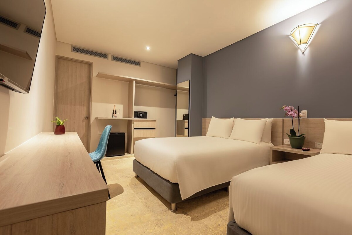 Moderni hotellihuone, jossa on kaksi sänkyä, työpöytä, tuoli, pieni keittokomero ja suuri peili.