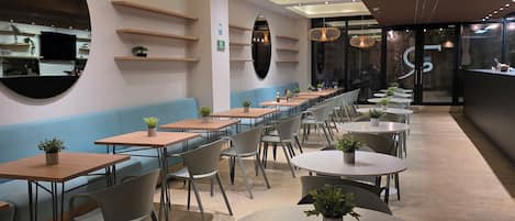A modern restaurant with a long counter, round tables, and blue cushioned seating.