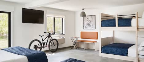 Ein Zimmer mit Etagenbetten, einem Fahrrad, einem Fernseher und einem Fenster mit Blick auf Bäume.