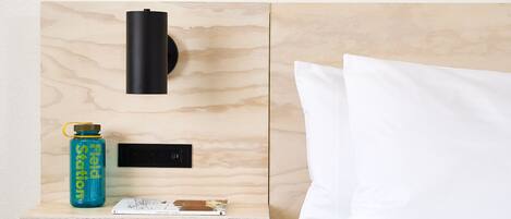 A wooden bedside table with a water bottle, a power outlet, and a book.