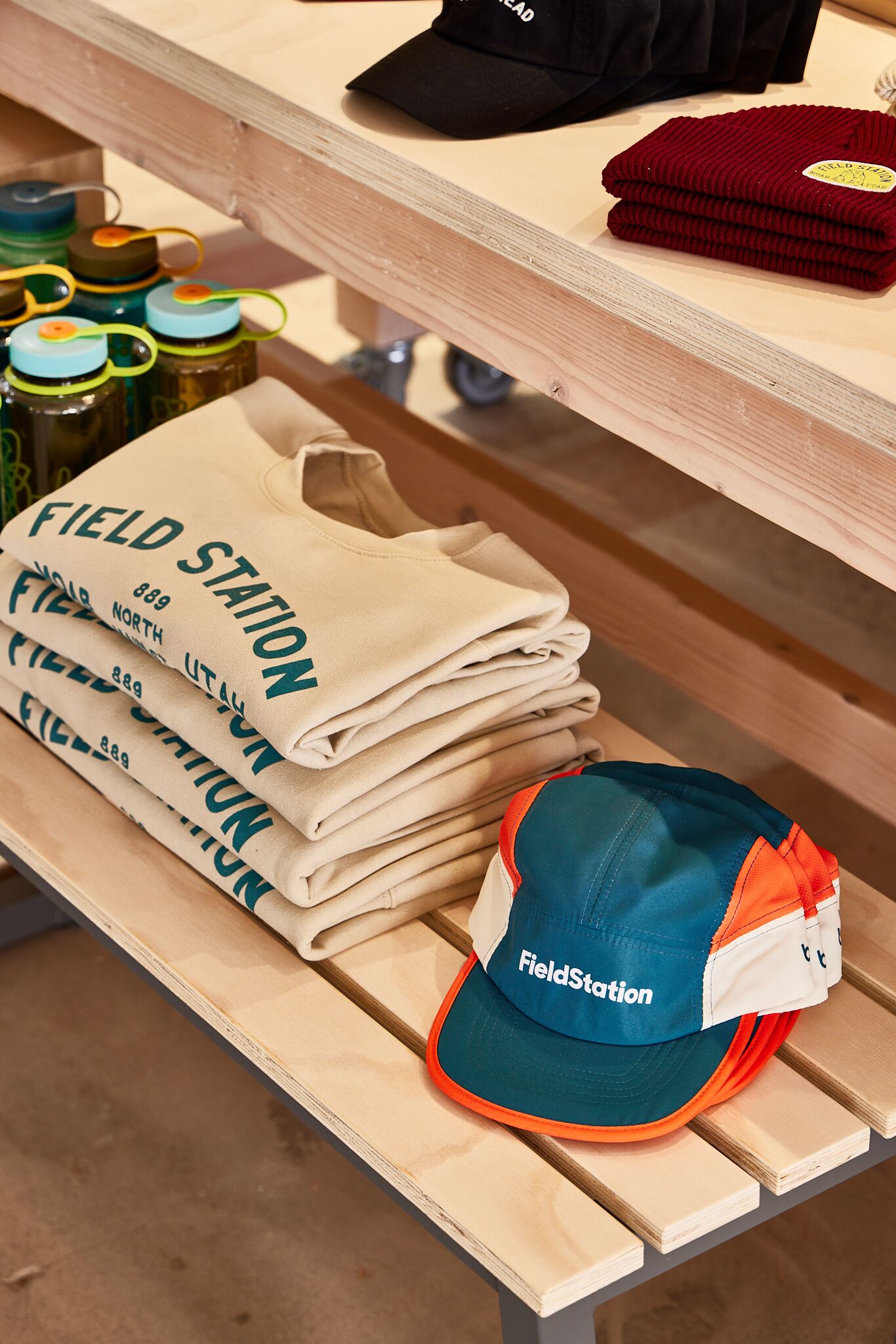 A wooden bench with folded beige t-shirts and a blue and orange cap with "FieldStation" text.