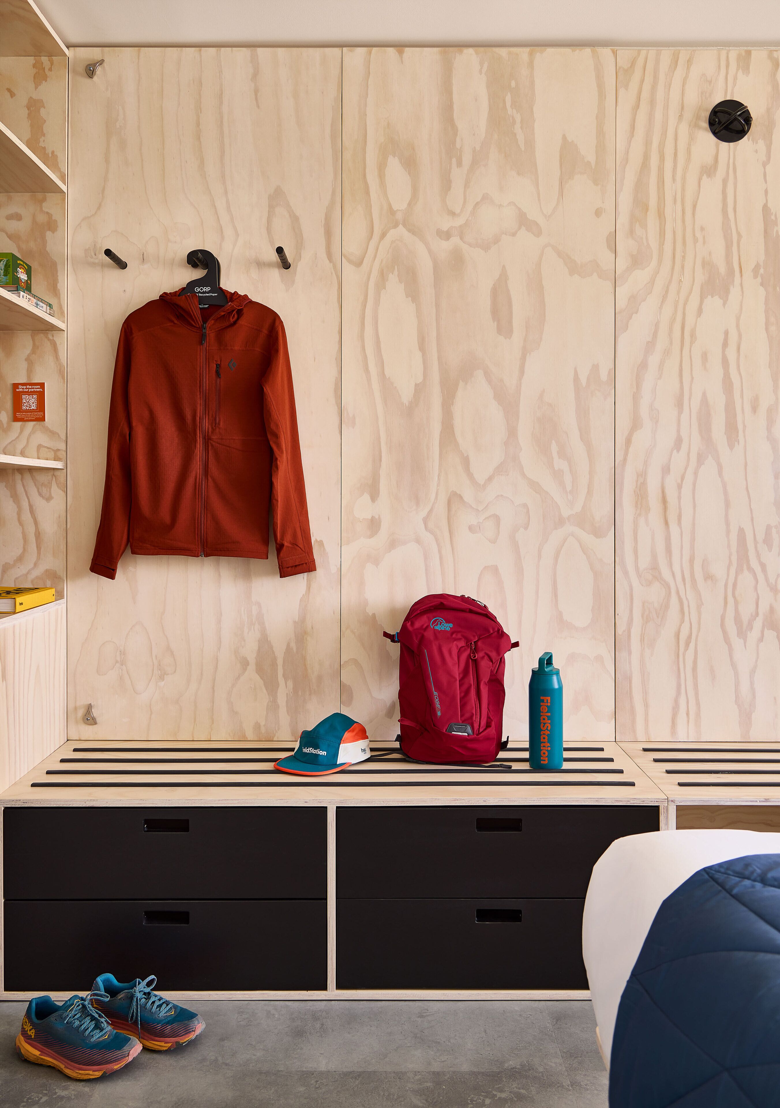 Une chambre avec une armoire en bois, un lit, une étagère sur laquelle se trouvent une veste, un sac à dos, une bouteille d’eau et une paire de chaussures.