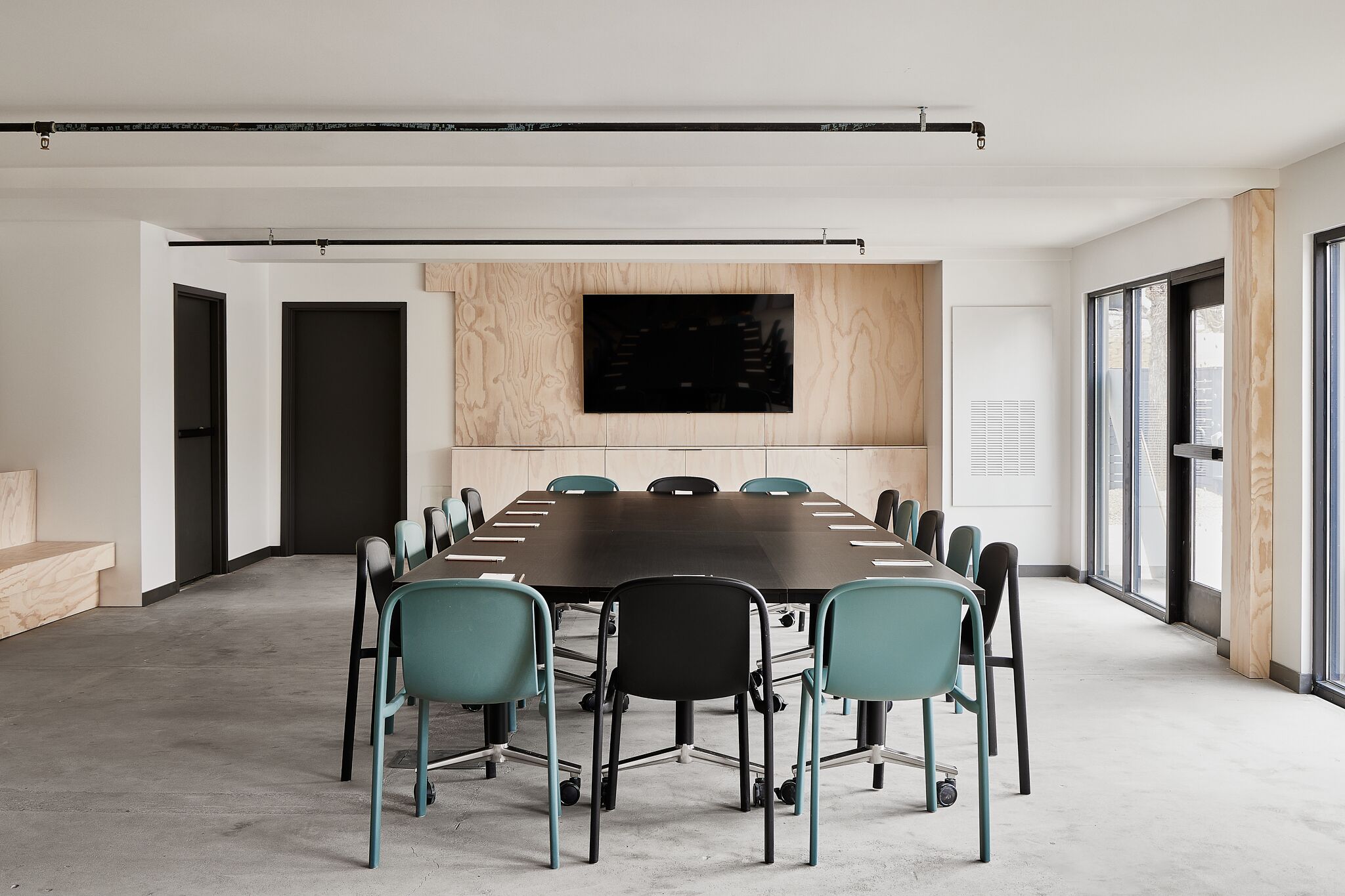 A conference room with a long table, teal chairs, and a large flat-screen TV on the wall.
