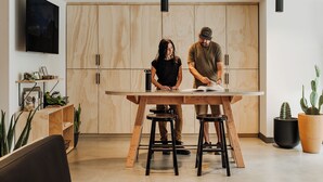 Una cocina moderna con armarios de madera, una mesa de comedor y dos personas trabajando en ella.