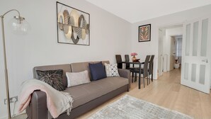 Ett modernt vardagsrum med en grå soffa, ett soffbord och en matplats med stolar. Det finns en golvlampa och konst på väggen.