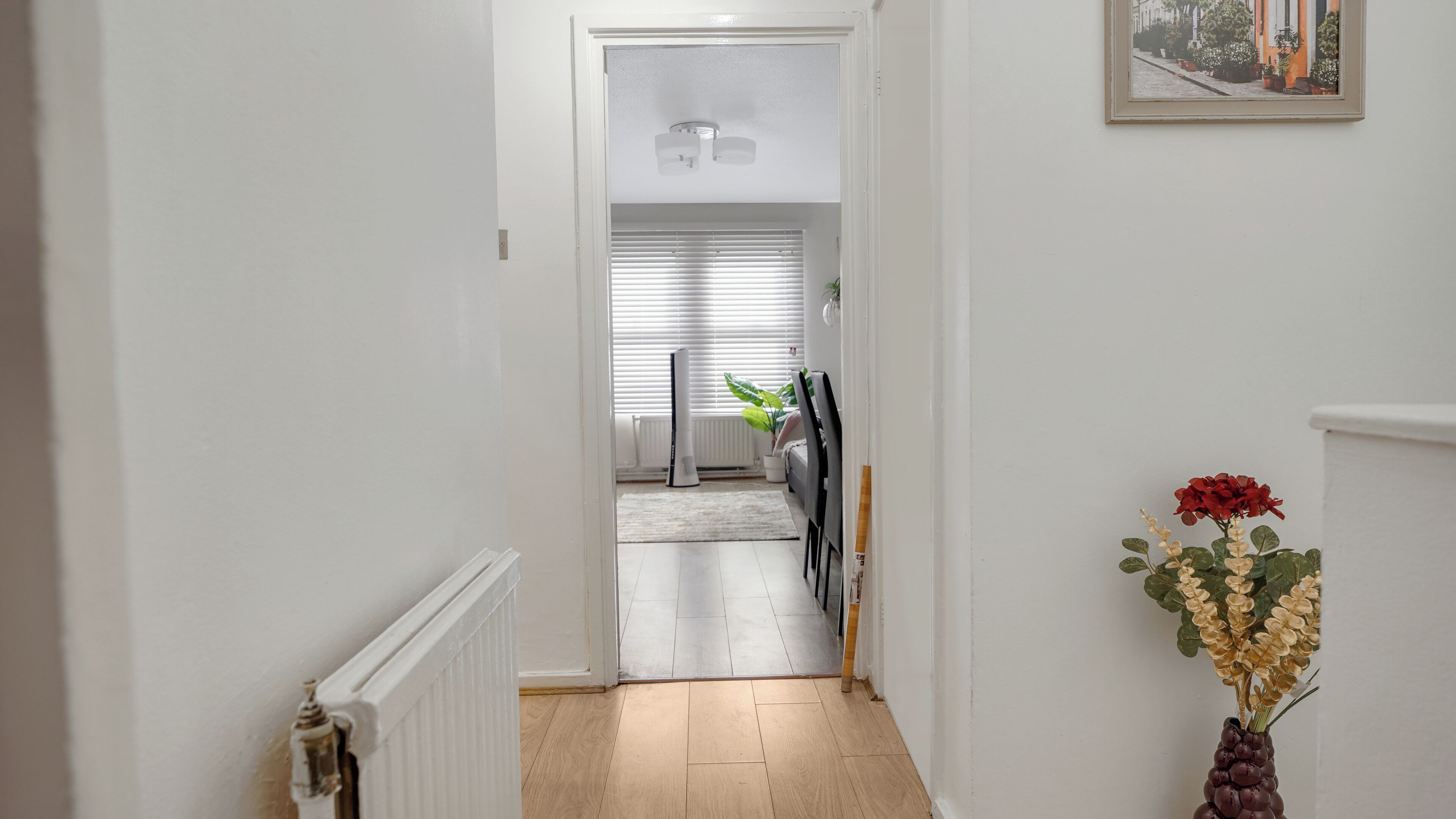 A hallway leading to a room with a radiator, a ceiling fan, and a framed picture on the wall.