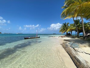 Ein unberührter tropischer Strand mit einem Segelboot in der Nähe des Ufers, Palmen und einem sandigen Strand.