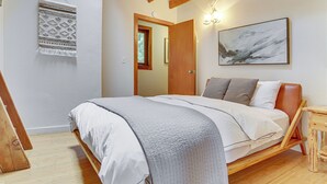 A bedroom with a wooden bed frame, white bedding, a gray throw blanket, a wooden nightstand, and a wall-mounted light fixture. - Mt. Hood Alpine Chalet w/ hot tub, kid & dog friendly (Rhododendron)