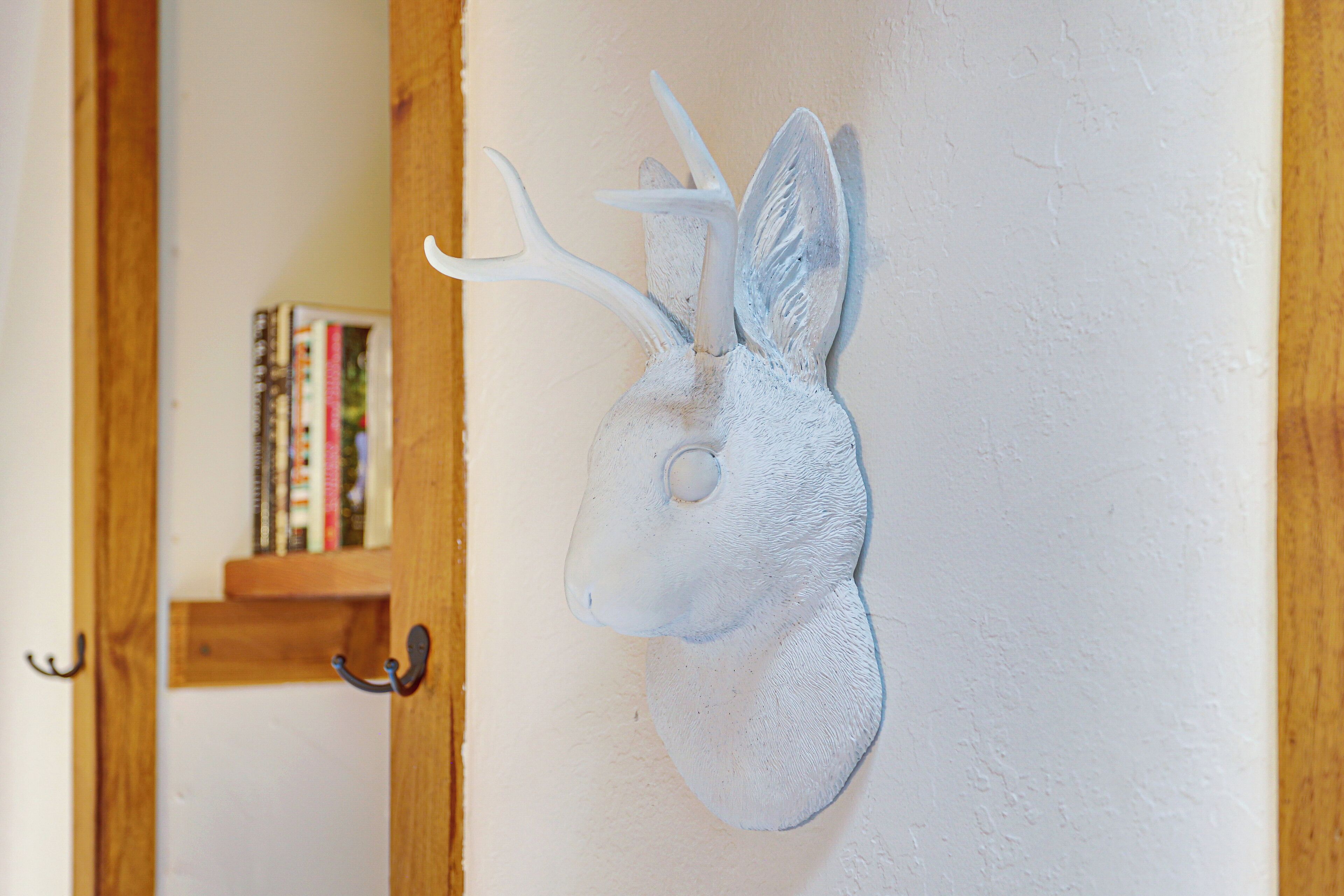 Une tête de cerf fixée au mur, avec une porte en bois et une bibliothèque en arrière-plan.