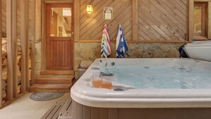 A wooden cabin with a stone wall, a wooden door, a hot tub, and two flags. - Mt. Hood Alpine Chalet w/ hot tub, kid & dog friendly (Rhododendron)