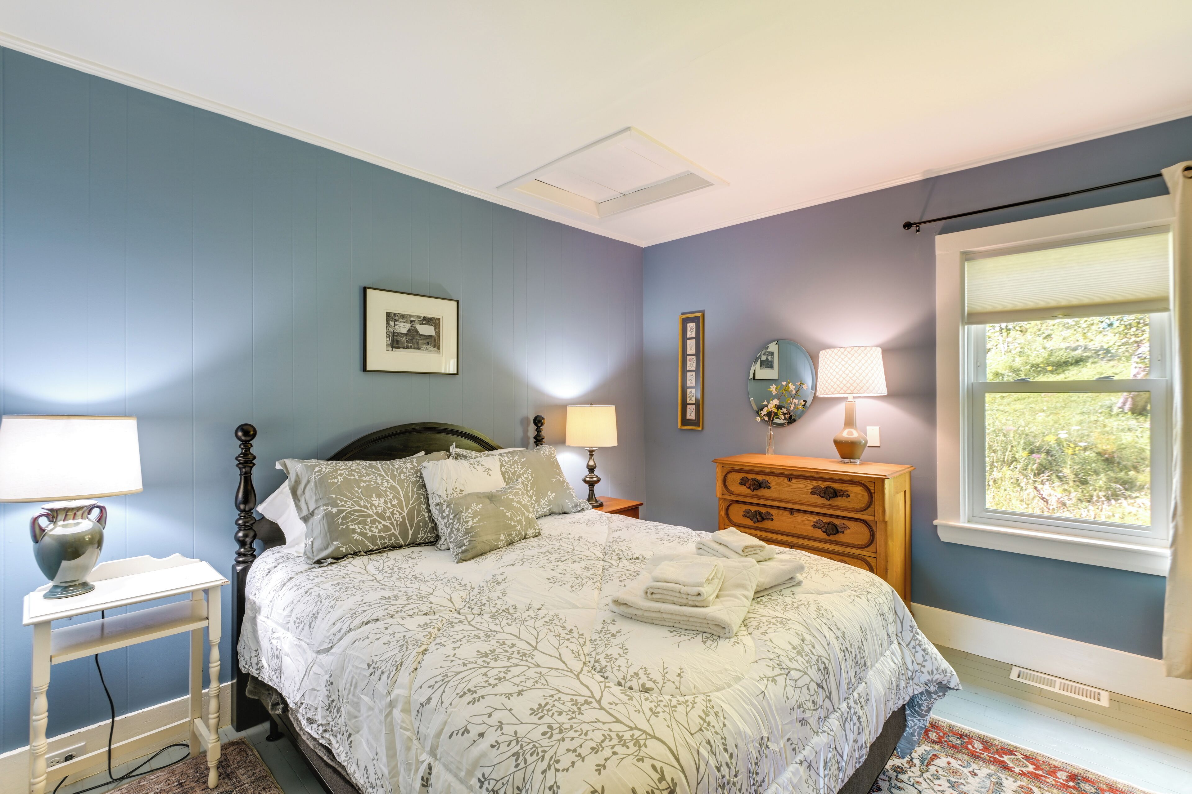 A bedroom with a bed, bedside tables, a dresser, a window with a view, and a ceiling light.