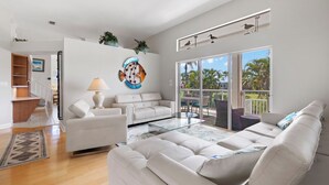 Un salón espacioso con un sofá blanco, una mesa de centro de vidrio y un ventanal con vistas a palmeras.
