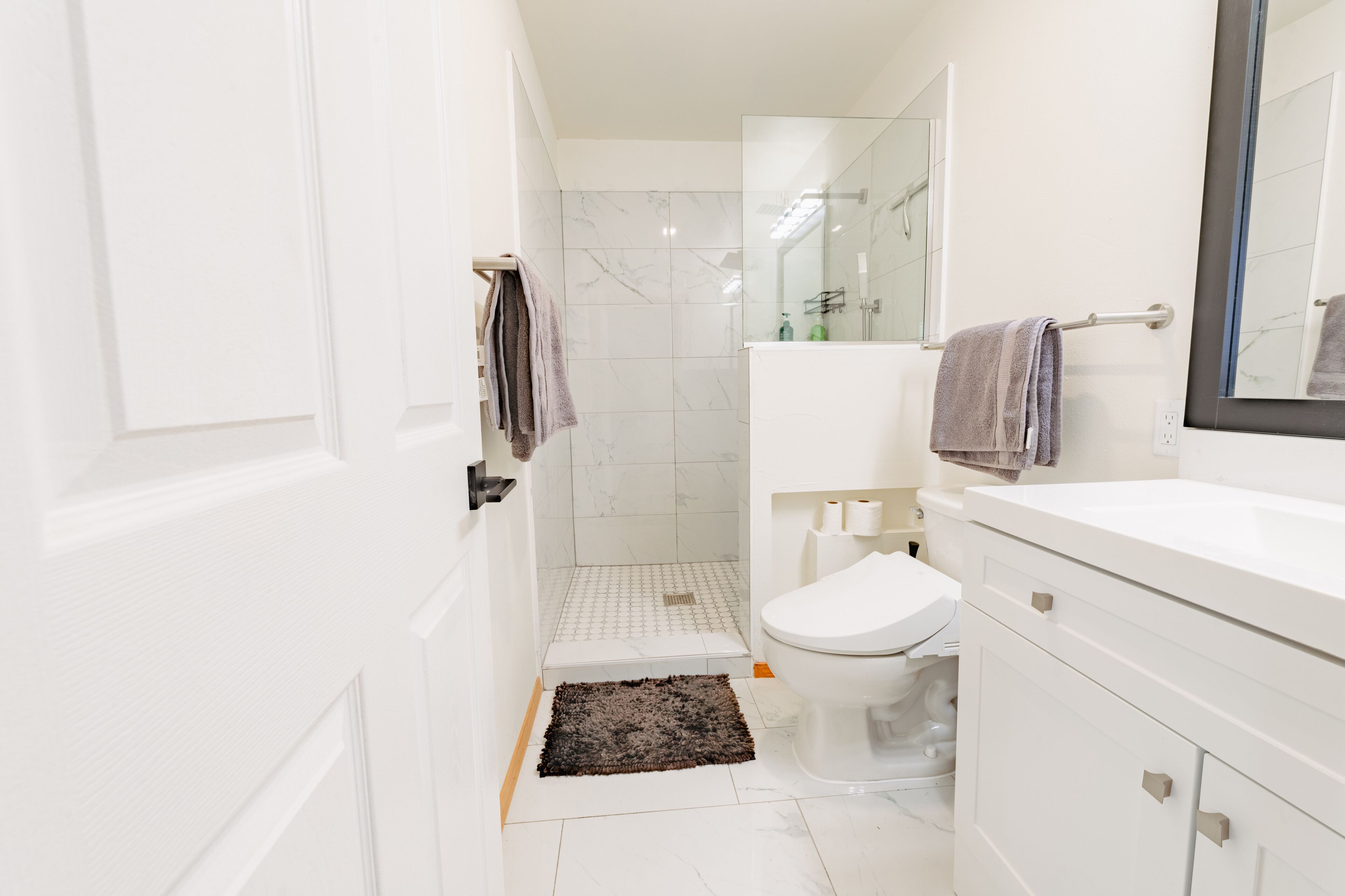 Een moderne badkamer met een wit toilet, een douchegedeelte en een wastafel met spiegel.