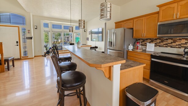 A modern kitchen with wooden cabinets, stainless steel appliances, and a large island with bar stools. - Family & Business • Minutes to Spokane Airport, • Fairchild AFB & Northern Quest (Spokane)