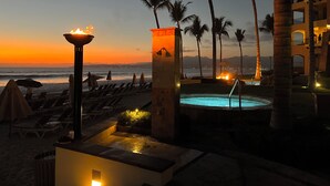 Un resort frente a la playa con piscina, sillas de descanso y vistas al atardecer.