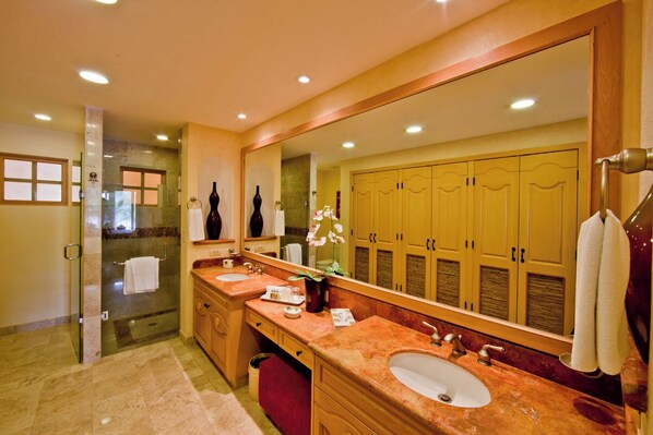 A modern bathroom with a large mirror, two sinks, a glass shower enclosure, and wooden cabinets. - PENTHOUSE VIEWS! BradAndJoeyRentals Sunsets, beach & city lights (Nuevo Vallarta)