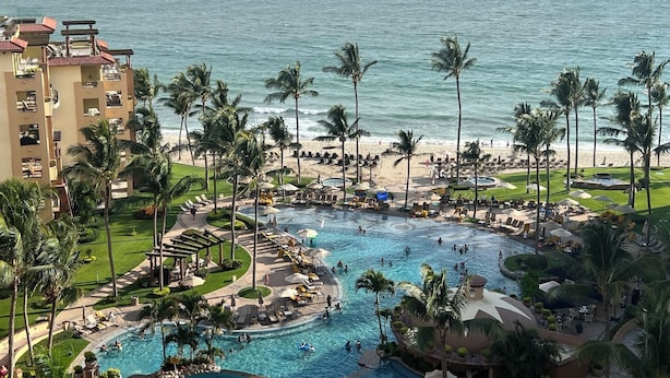 Un resort con una amplia piscina, palmeras y vistas a la playa.