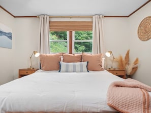 A bedroom with a large bed, two bedside tables with lamps, a window with curtains, and a wall-mounted decorative item. - Ray's Mtn Retreat ~ Hot Tub+Fire Pit, WiFi, Grill! (Green Mountain)