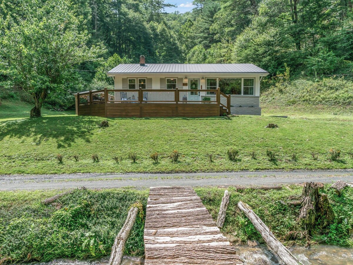 A house with a wooden deck, surrounded by a grassy field and trees.