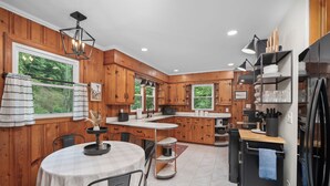 A modern kitchen with wooden cabinets, a central island, and a dining area with a round table and chairs. - Charming Mtn Cabin, Hot Tub+Fire Pit, Private, WiFi, Grill, Near Green Mtn Area! (Green Mountain)