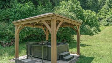 A wooden gazebo with a built-in hot tub and steps leading up to it.