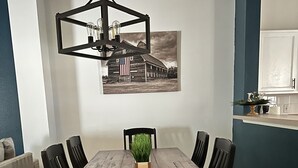 A dining area with a wooden table, black chairs, a hanging light fixture, and a wall-mounted picture. - Modern Disney Retreat! 2 Pools + Prime location (Kissimmee)