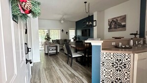 A modern kitchen with a central island, a dining area with a table and chairs, and a living room with a sofa and a coffee table. - Modern Disney Retreat! 2 Pools + Prime location (Kissimmee)