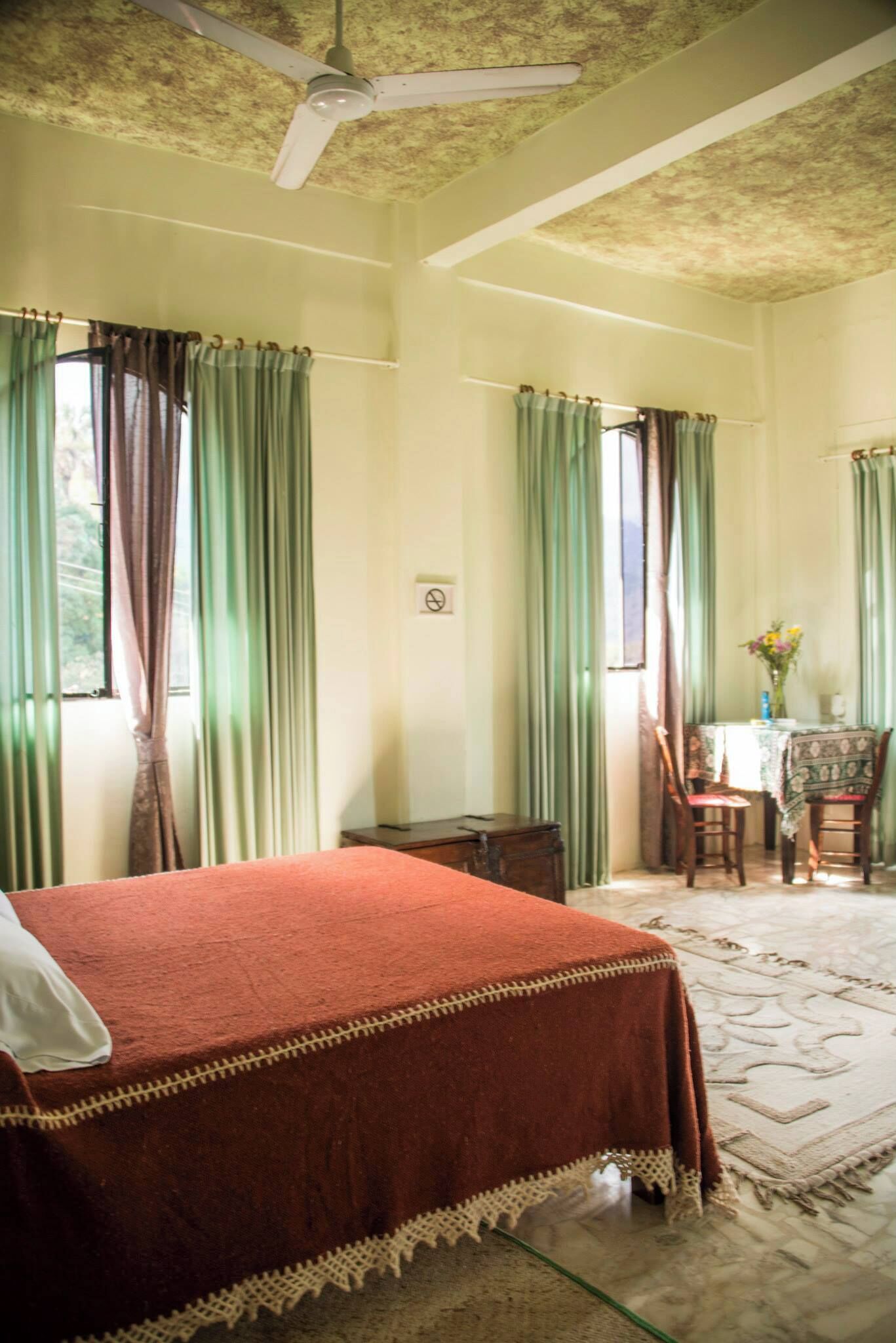 Una habitación con cama, una mesa con sillas, un ventilador de techo y cortinas.