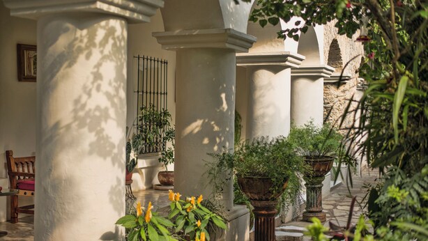Ein Innenhof mit Säulen, Blumentöpfen und einer Bank.