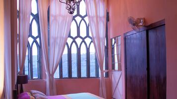 A room with two beds, a chandelier, and large windows with curtains.