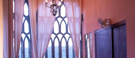 A room with two beds, a chandelier, and large windows with curtains.
