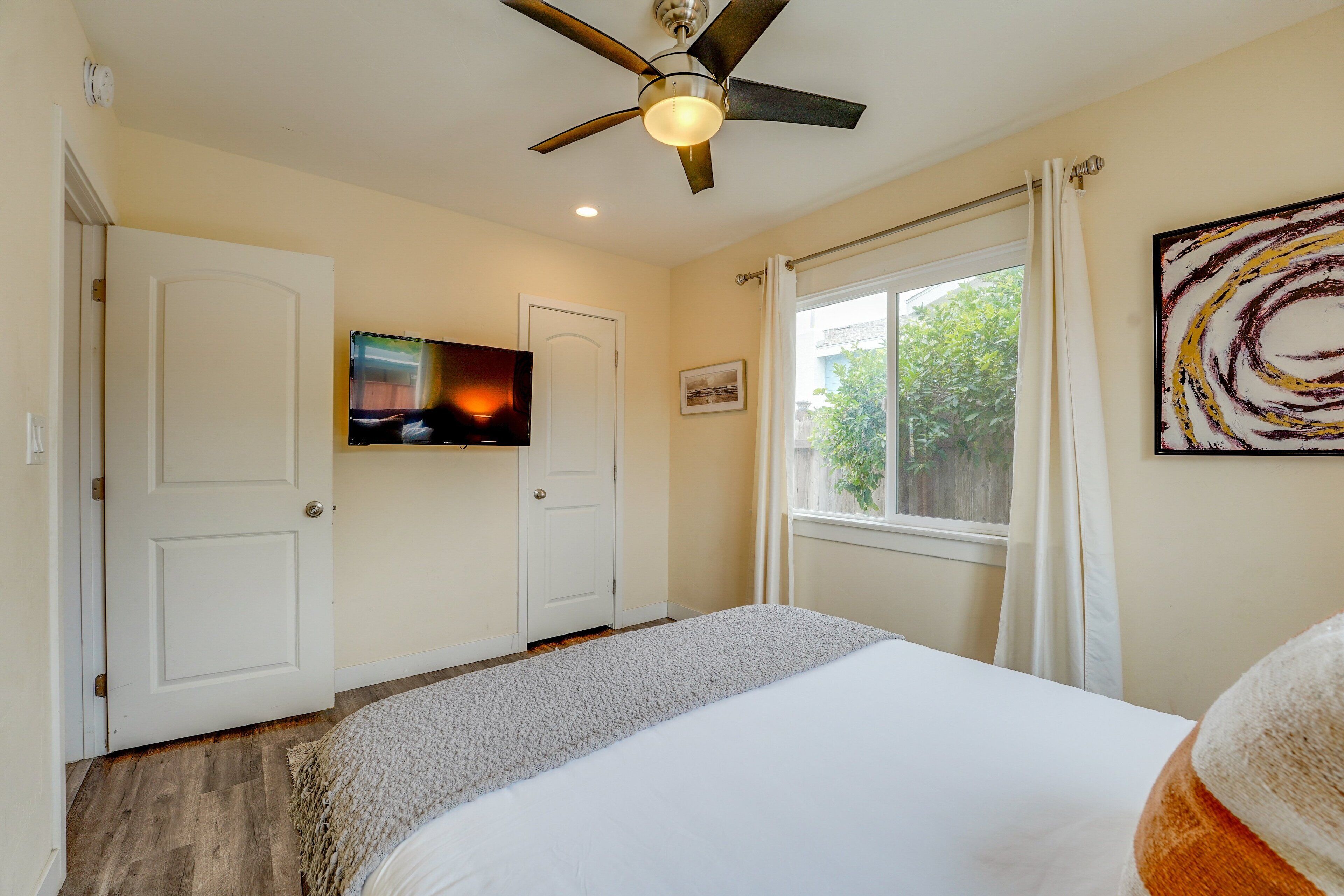 A bedroom with a bed, a ceiling fan, a TV, and a window with curtains.
