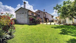 A stone building with a chimney, a garden with flowers, and a clear blue sky. - Villa with pool and volleyball court (Barban)
