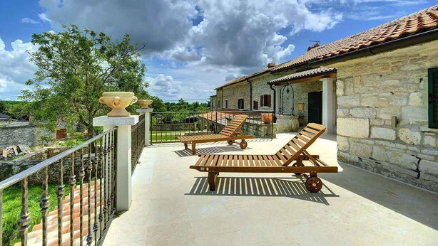 A stone building with a tiled roof, a balcony with wooden lounge chairs, and a decorative urn. - Villa with pool and volleyball court (Barban)
