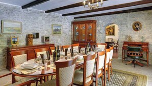 A dining room with a round table set for six, surrounded by wooden chairs. A wooden cabinet with glass doors is against the stone wall. - Villa with pool and volleyball court (Barban)