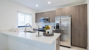 Een moderne keuken met een groot eiland, roestvrijstalen apparatuur en houten kastjes.