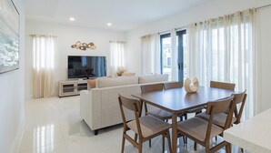 Een moderne woonkamer met een bank, televisie en een eettafel met stoelen.