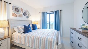 Een slaapkamer met een bed, nachtkastjes, een dressoir en een raam met gordijnen.